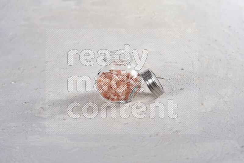 A glass jar full of coarse himalayan salt crystals on white background