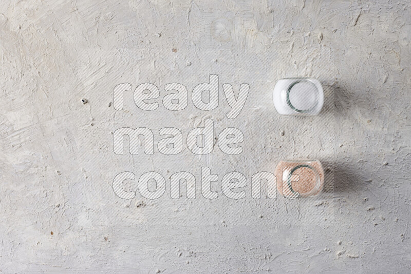 2 glass jars one is full of fine himalayan salt and the other with table salt on white background