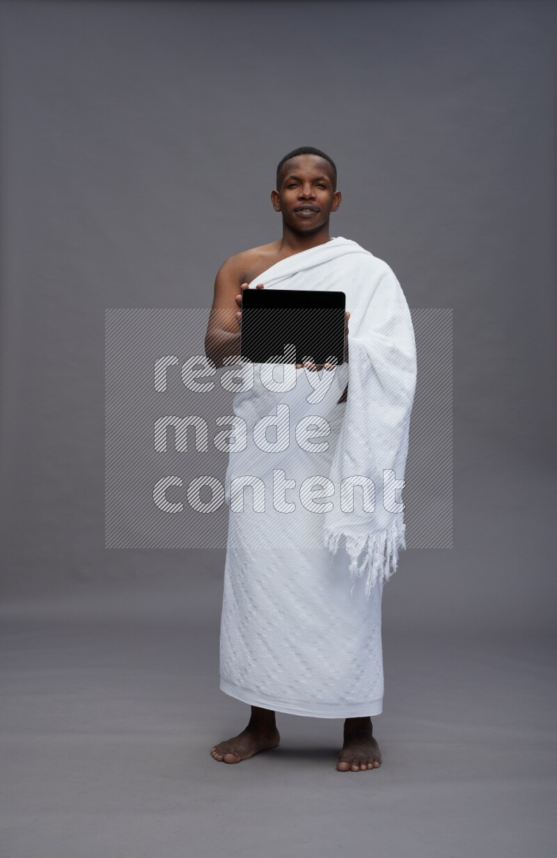 A man wearing Ehram Standing showing tablet to camera on gray background