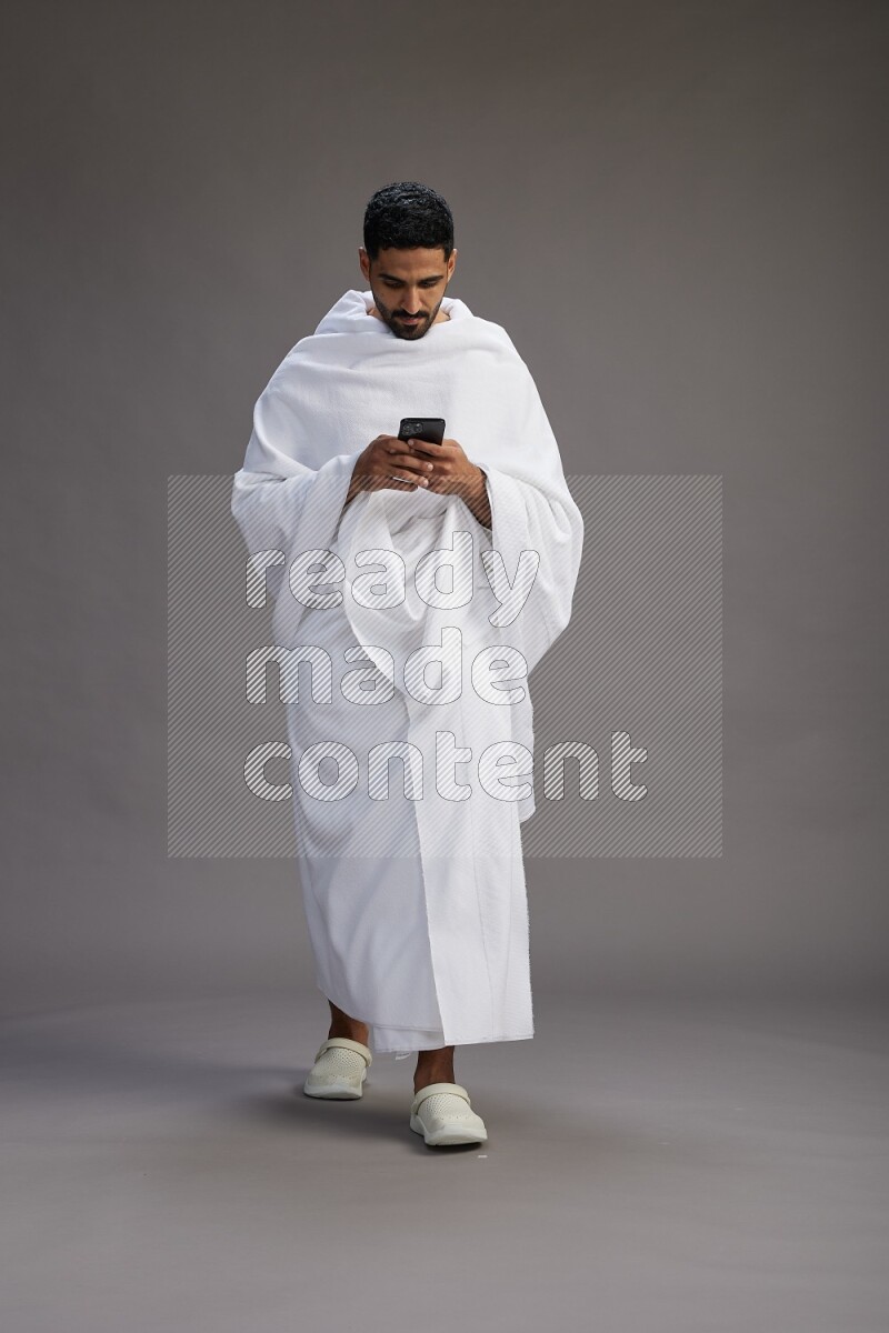 A man wearing Ehram Standing texting on phone on gray background