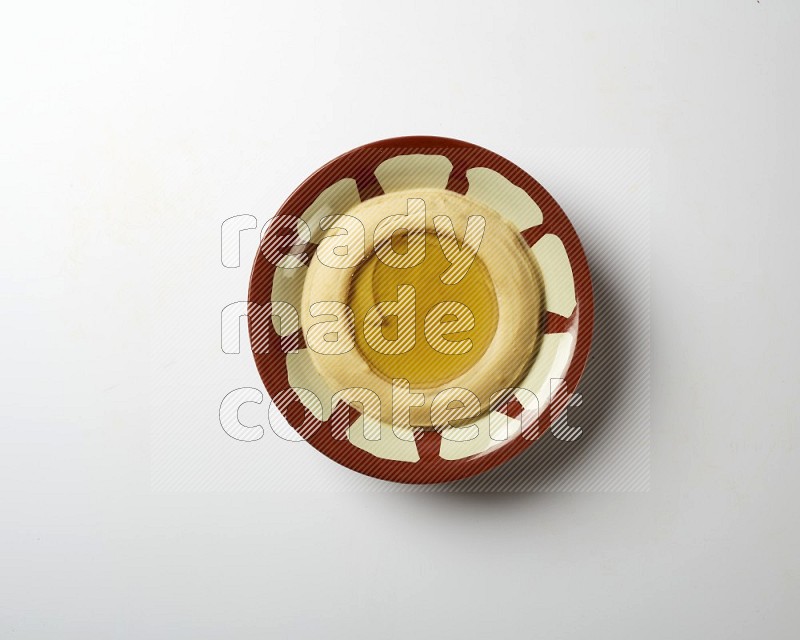 Hummus in a traditional plate garnished with olive oil on a white background