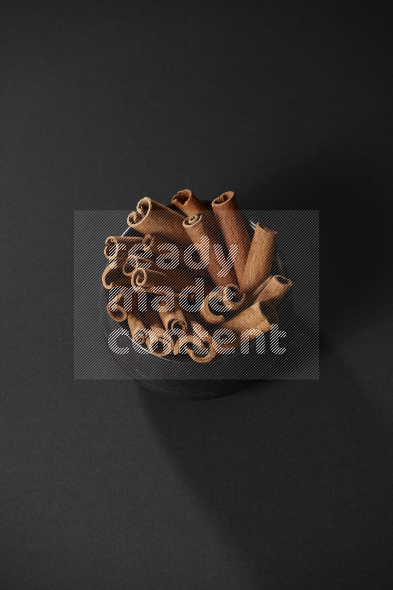 Cinnamon sticks in a black bowl on a black background in different angles
