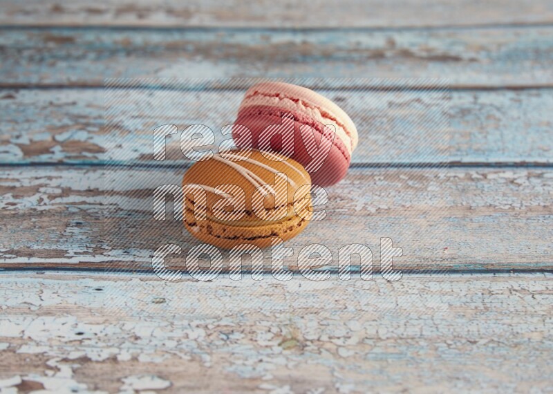 45º Shot of of two assorted Brown Irish Cream, and Pink Litchi Raspberry macarons on light blue background