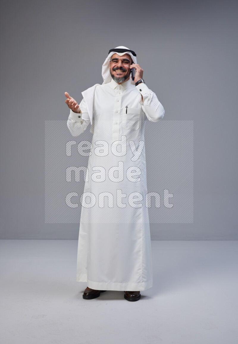 Saudi man Wearing Thob and white Shomag standing talking on phone on Gray background