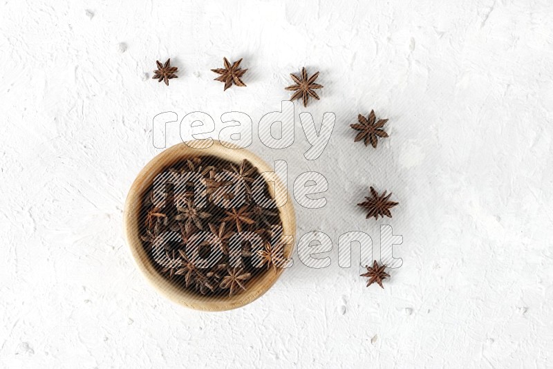Star anise in a wooden bowl with more anise on the floor on white background