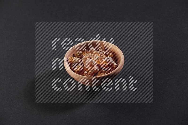 A wooden bowl full of gum arabic on a black flooring