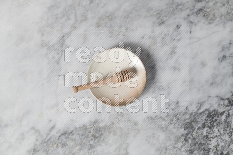 Beige pottery plate with wooden honey dipper in it on grey marble background