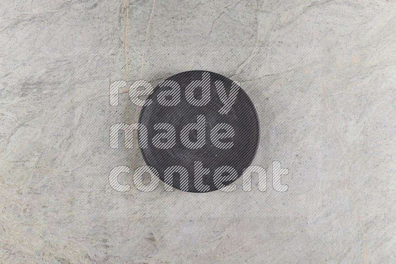 Top View Shot Of A Black Pottery Circular Plate On Grey Marble Flooring