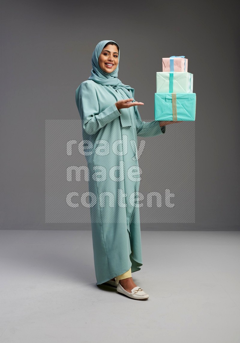 Saudi Woman wearing Abaya standing holding gift box on Gray background