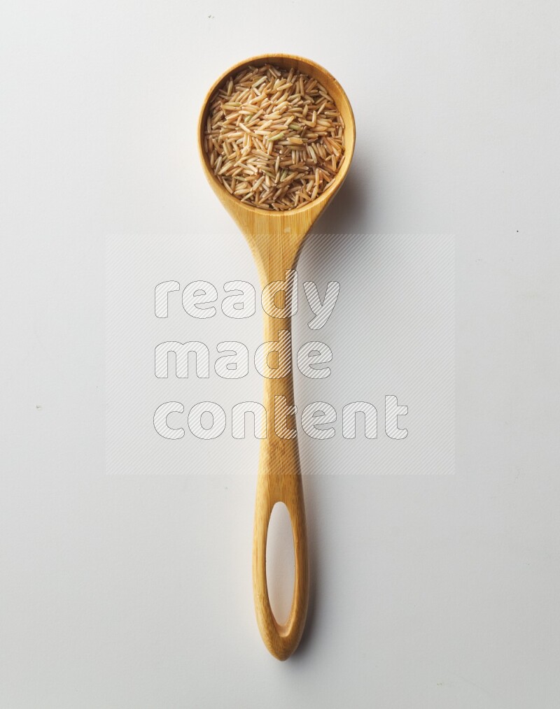 Top-view of a long grain brown rice inside a wooden spoon on white background