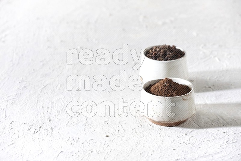 2 Beige ceramic bowls, one full of cloves and the other full of powder on textured white flooring