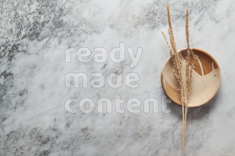 Wheat stalks on multicolored pottery plate on grey marble background