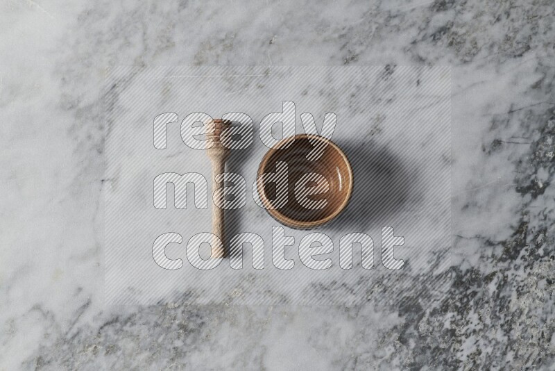 Brown pottery bowl with wooden honey dipper on the side on grey marble background