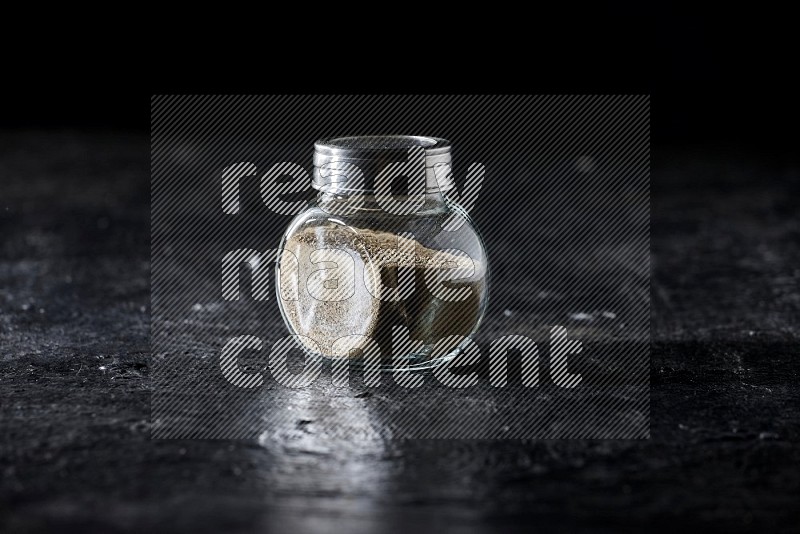 Herbal glass jar full of white pepper on textured black flooring