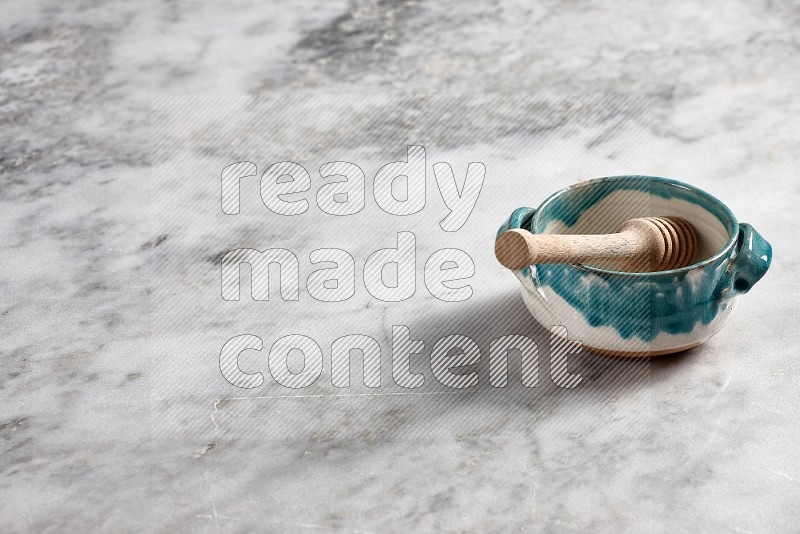 Multicolored Pottery bowl with wooden honey handle in it, on grey marble flooring, 45 degree angle