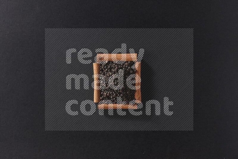 A single square of cinnamon sticks full of black pepper on black flooring