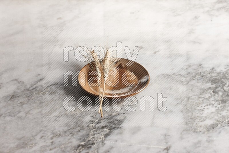 Wheat stalks on multicolored pottery plate on grey marble background