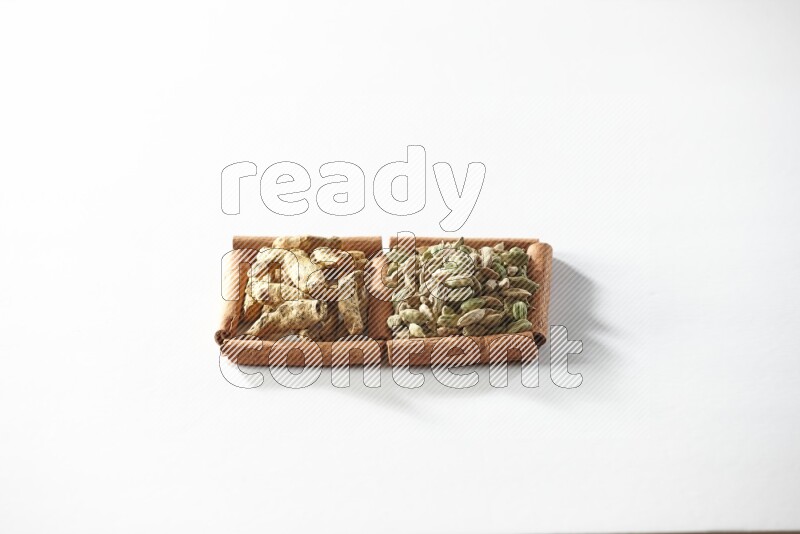 مربعان من أعواد القرفة ممتلئان بحبوب الهيل وأصابع الكركم علي خلفية بيضاء