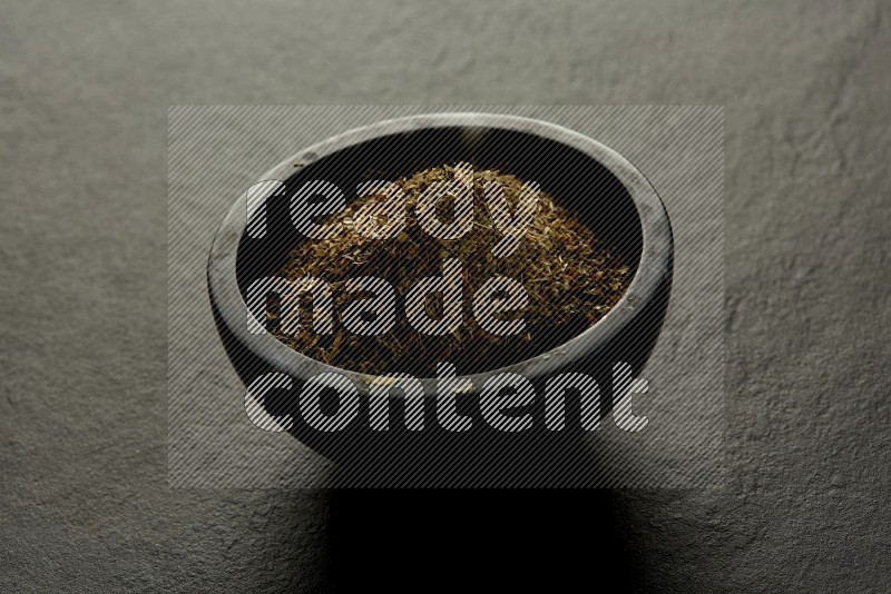 black pottery round sauce bowl filled with herbs on grey textured countertop