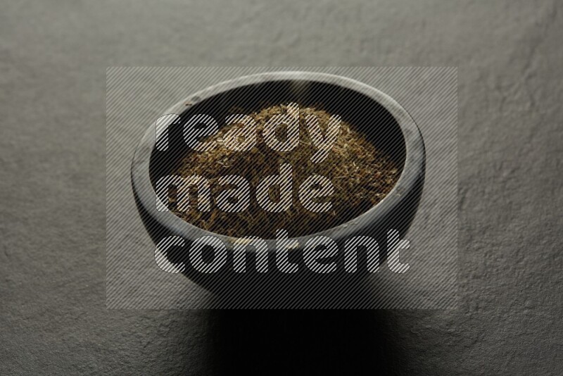 black pottery round sauce bowl filled with herbs on grey textured countertop