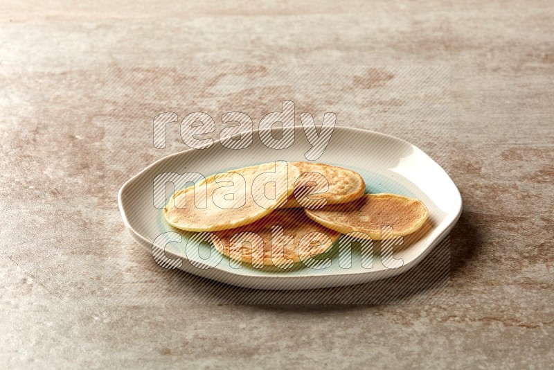 Four stacked plain mini pancakes in a bicolor plate on beige background