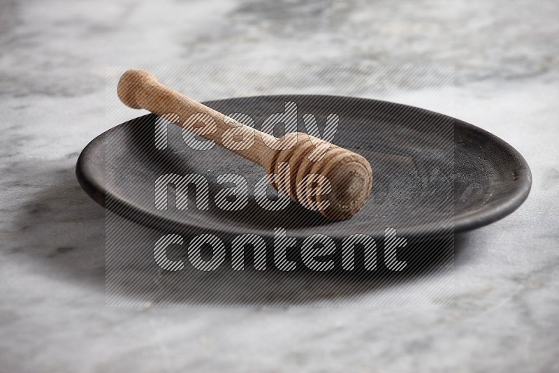 Black Pottery Plate with wooden honey handle in it, on grey marble flooring, 15 degree angle