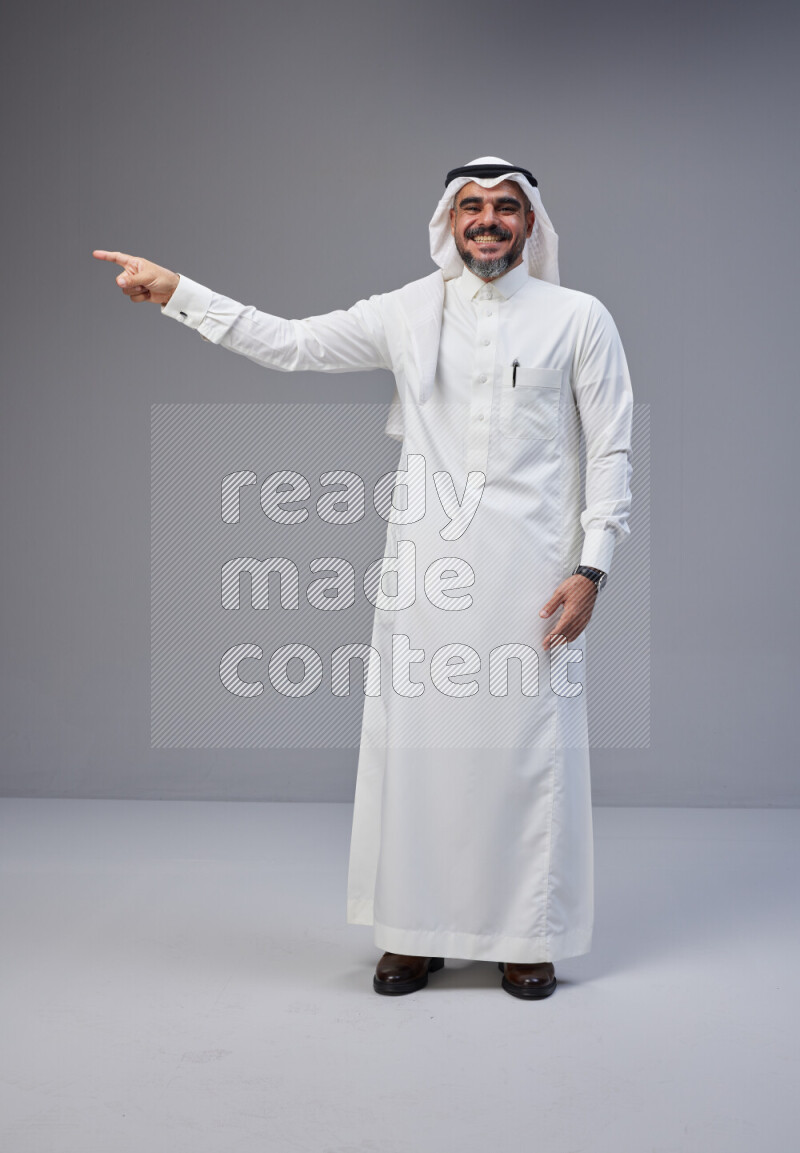 Saudi man Wearing Thob and white Shomag standing interacting with the camera on Gray background