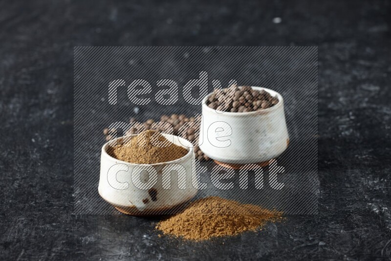 2 beige bowls, one full of allspice powder and the other full of whole balls and both spread on a textured black flooring