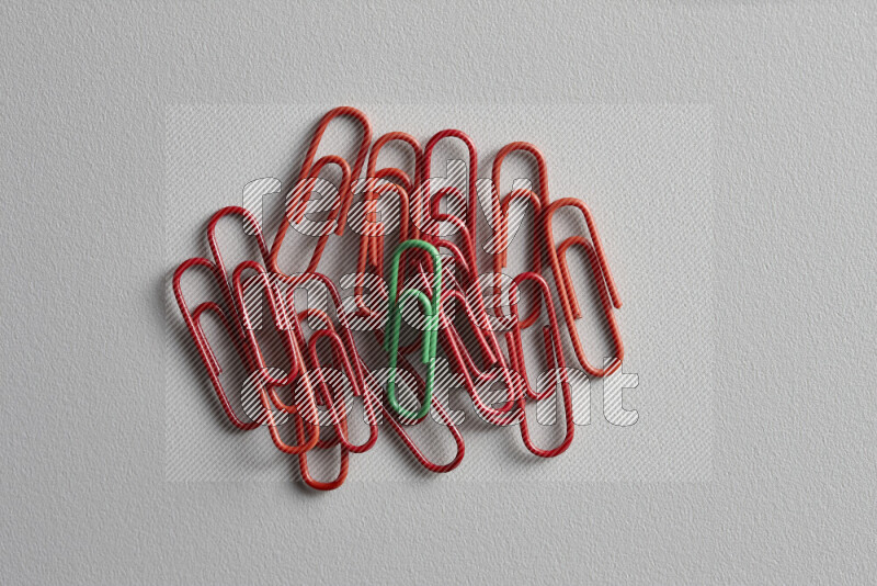 A bunch of red paper clips with a different colored paper clip in the center on grey background