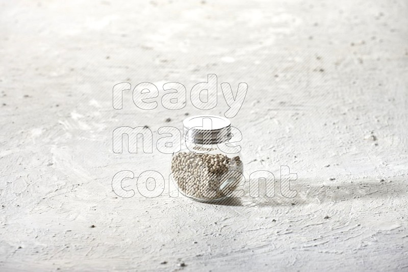 Herbal Glass jar full of white pepper beads on textured white flooring