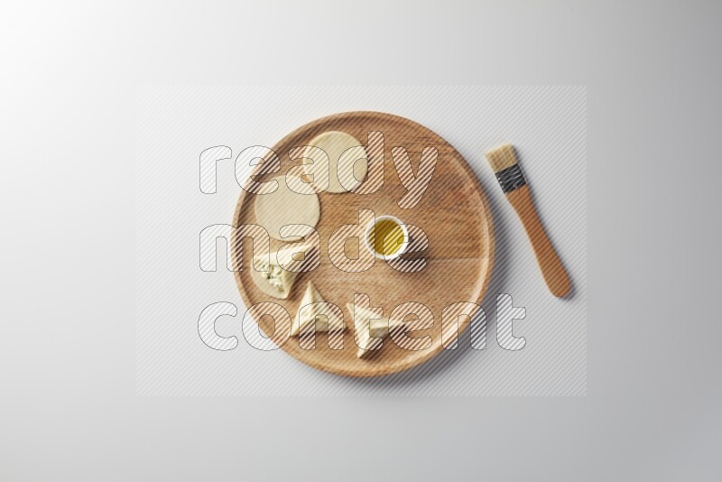 two closed sambosas and one open sambosa filled with cheese while oil with oil brush aside in a wooden dish on a white background