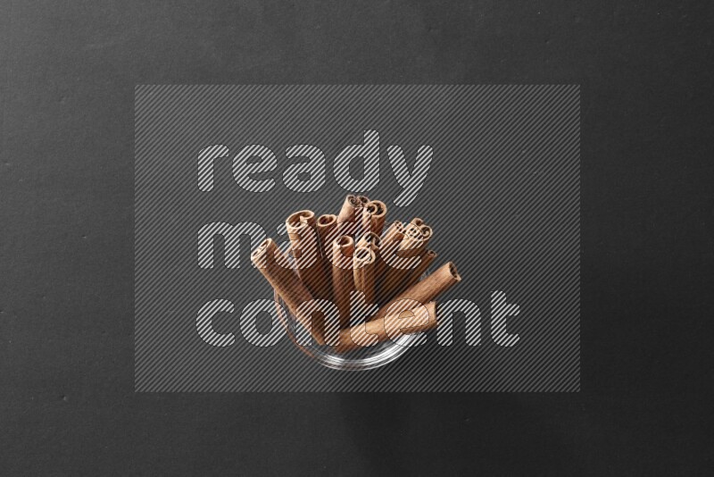 A glass bowl full of cinnamon sticks on black flooring