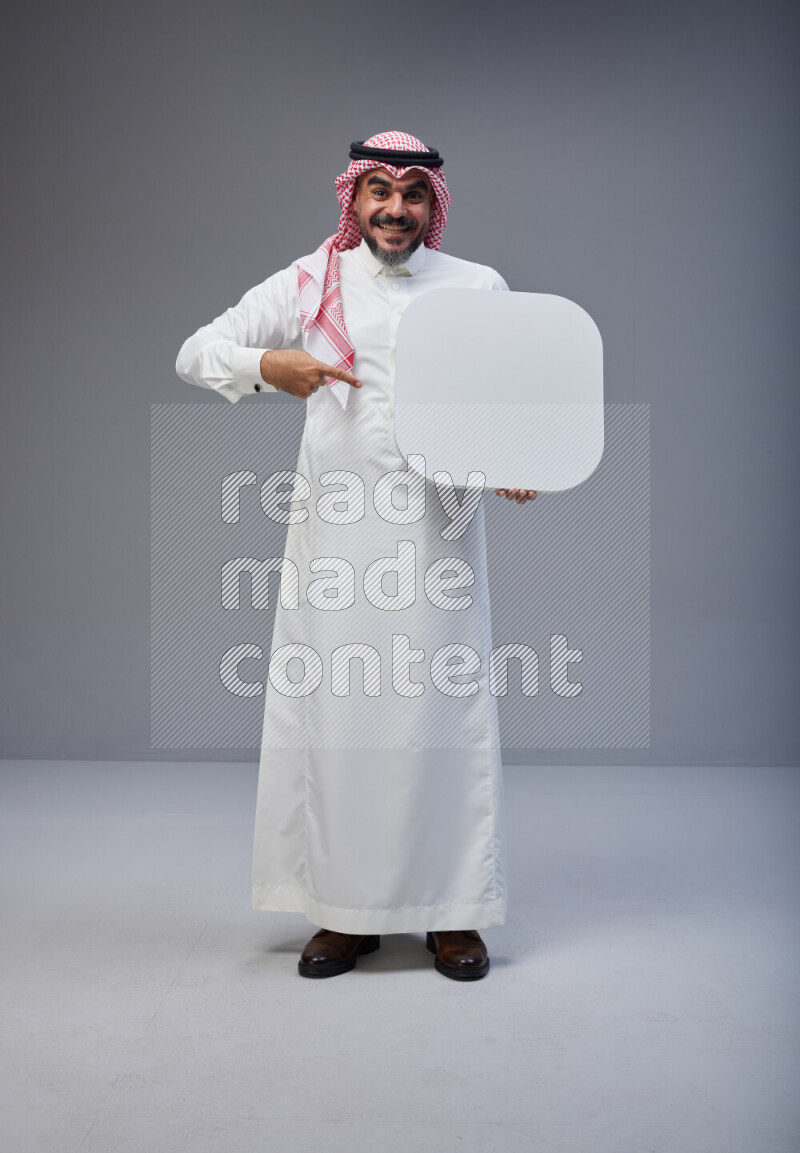 Saudi man Wearing Thob and red Shomag standing holding social media sign on Gray background