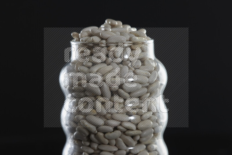 White beans in a glass jar on black background