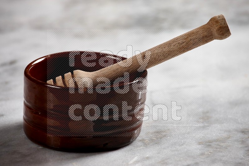Brown Pottery bowl with wooden honey handle in it, on grey marble flooring, 15 degree angle