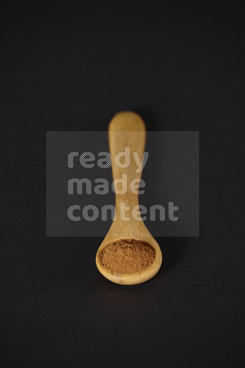 Cinnamon powder in a wooden spoon on a black background