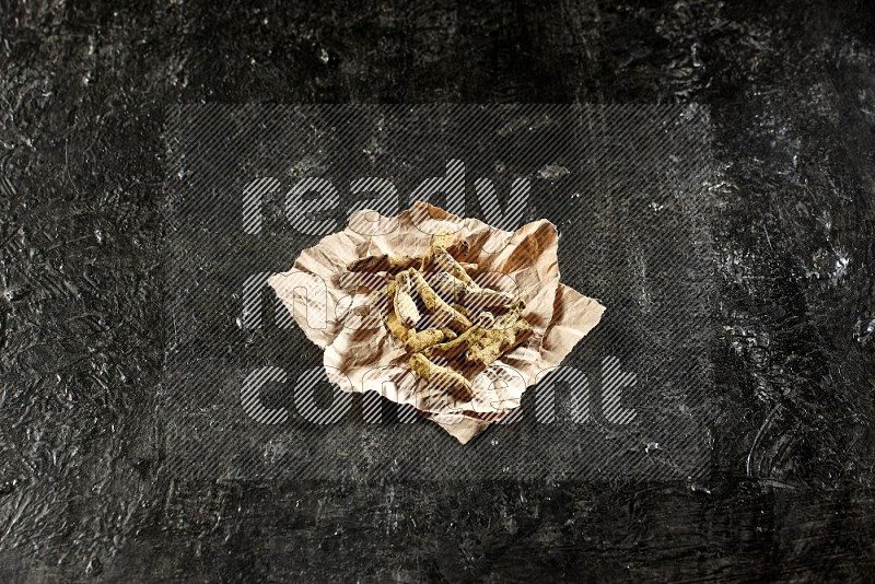 Dried turmeric whole fingers in a crumpled piece of paper on textured black flooring