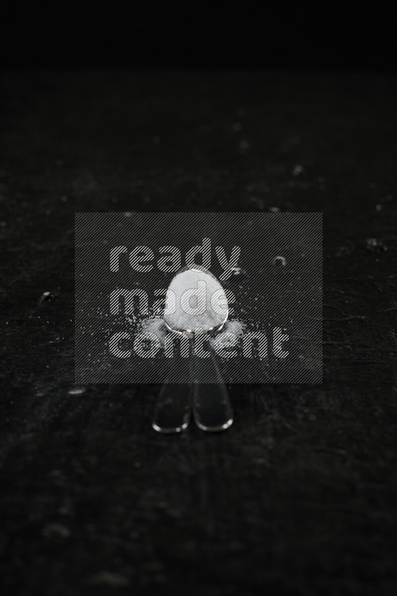 ملعقتان معدنيتان ممتلئتان بالملح الأبيض على خلفية سوداء