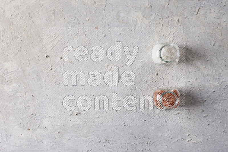 2 glass jars one is filled with coarse himalayan salt and the other with coarse sea salt on white background