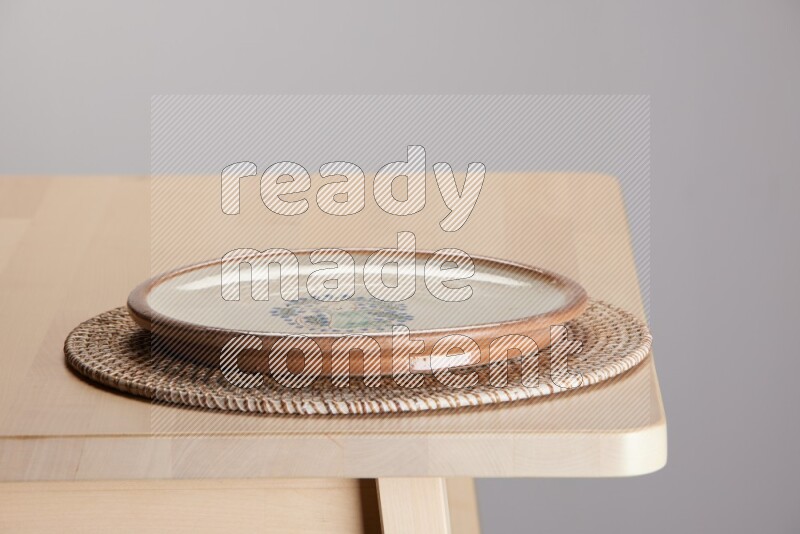 multi-colored pottery Plate placed on a big light colored straw placemat on the edge of wooden table
