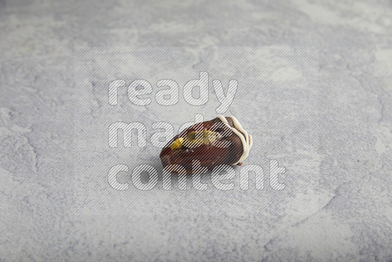 pistachio stuffed date covered with dark chocolate with white chocolate drizzle on a light grey background