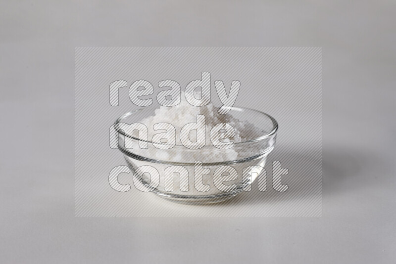 A glass bowl full of coarse sea salt crystals on white background