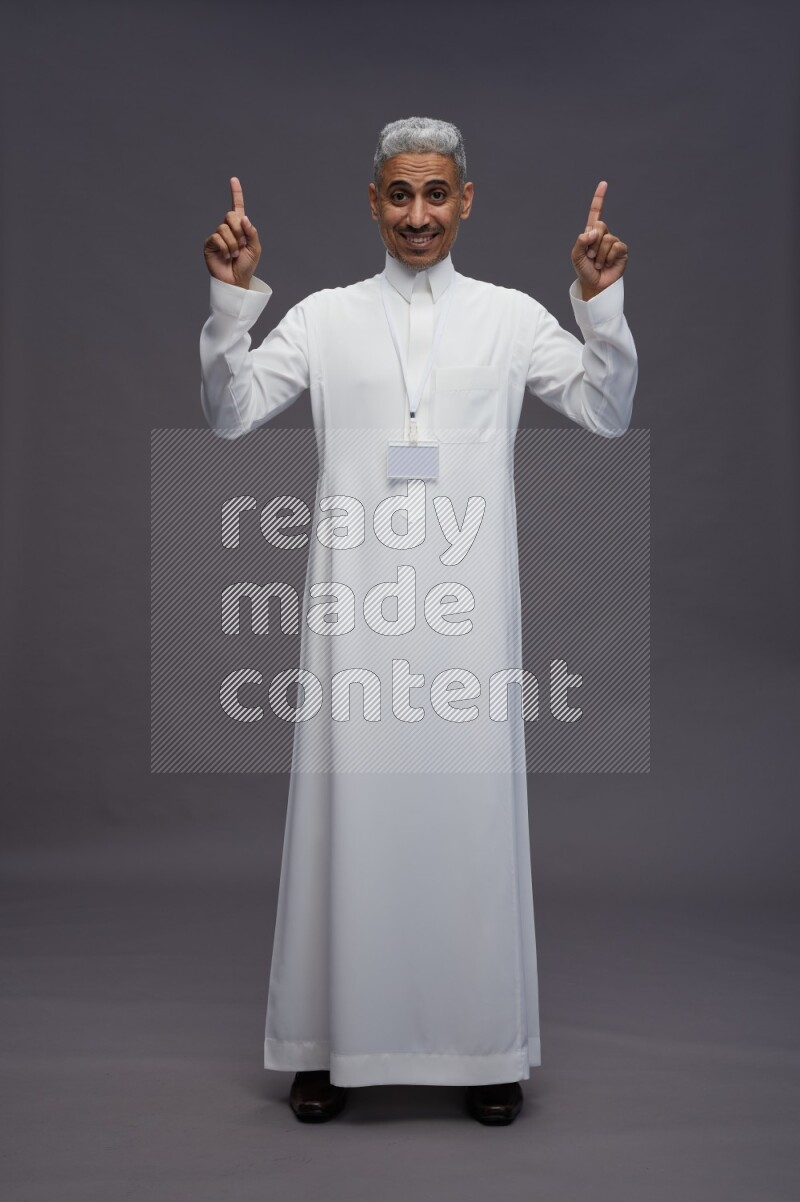 Saudi man wearing thob with neck strap employee badge standing interacting with the camera on gray background
