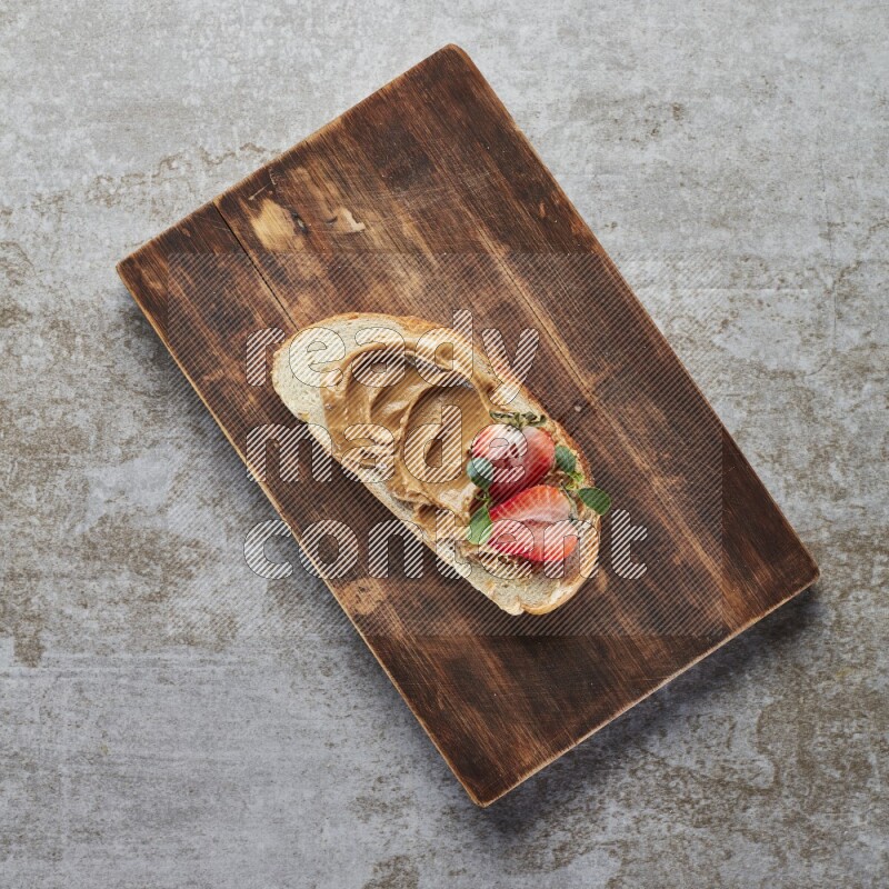 open faced peanut butter sandwich with strawberries on a grey textured background