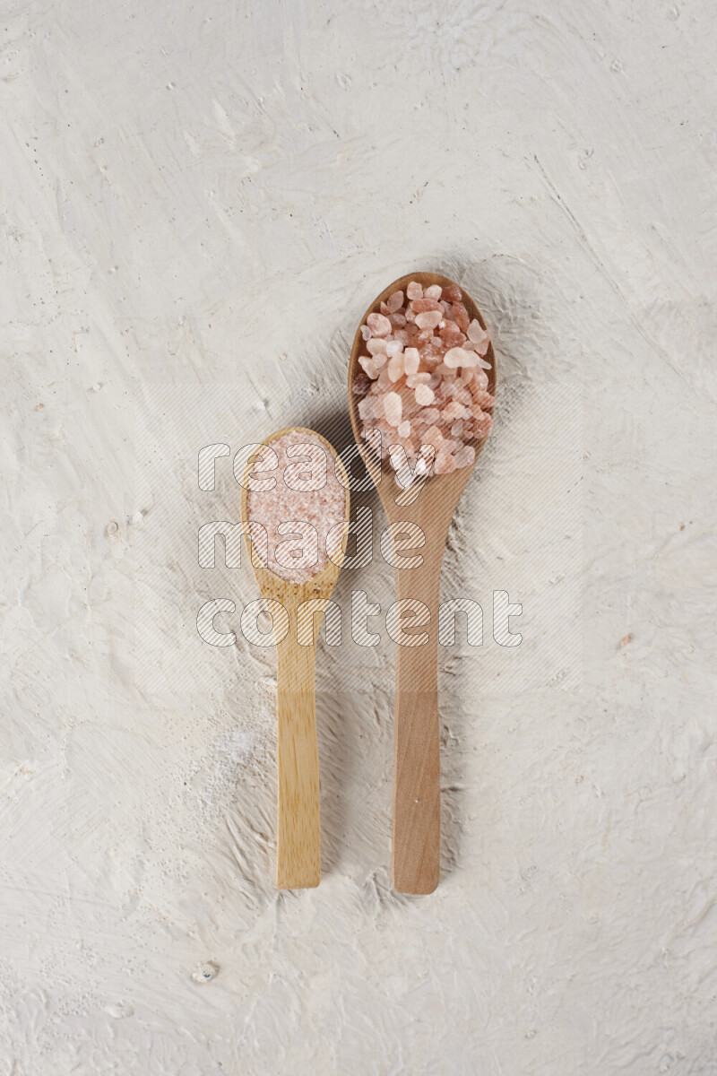 2 wooden spoons filled with fine and coarse salt on white background