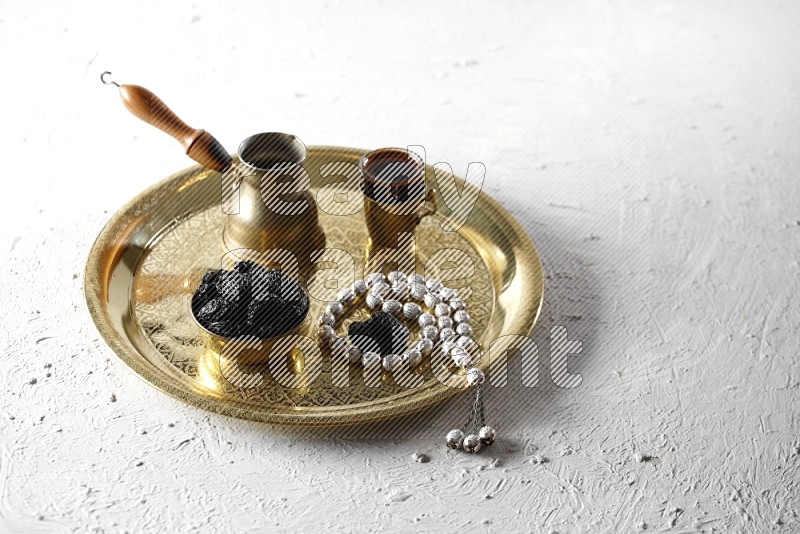 Dried plums in a metal bowl with coffee and prayer beads on a tray in a light setup