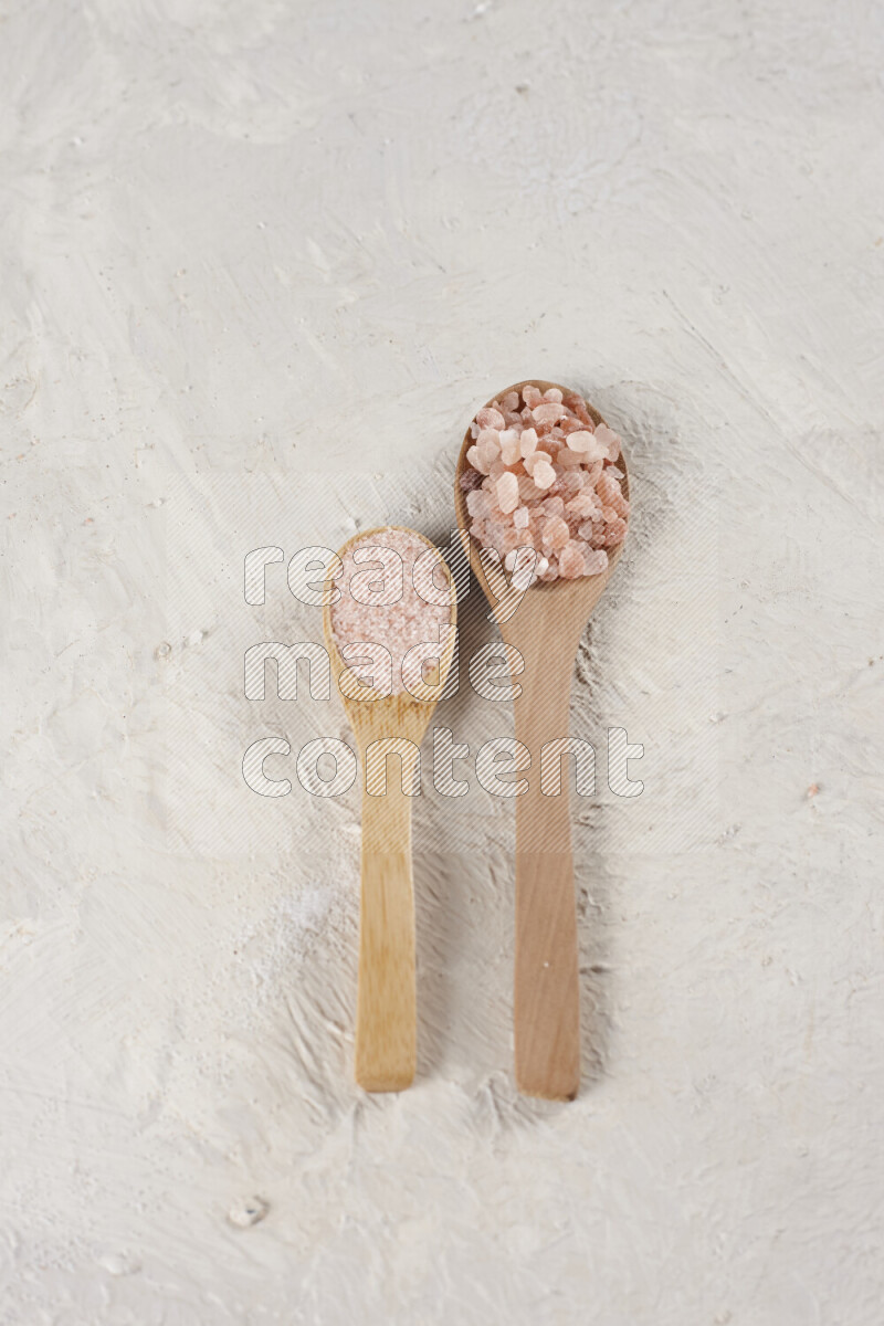 2 wooden spoons filled with fine and coarse salt on white background
