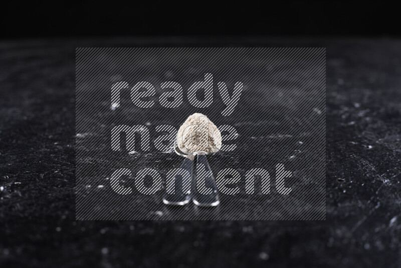 ملعقتان معدنيتان أحدهما ممتلئة ببودرة البصل علي خلفية سوداء