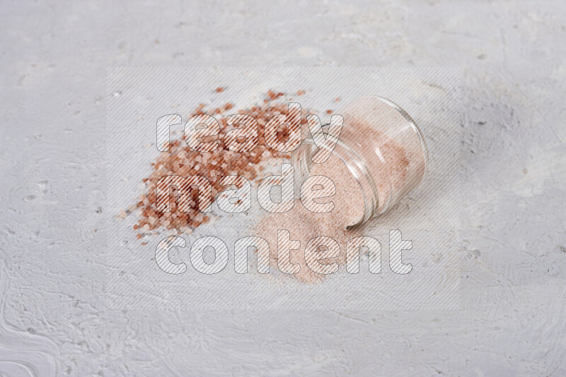 A glass jar full of fine himalayan salt with some himalayan crystals beside it on a white background