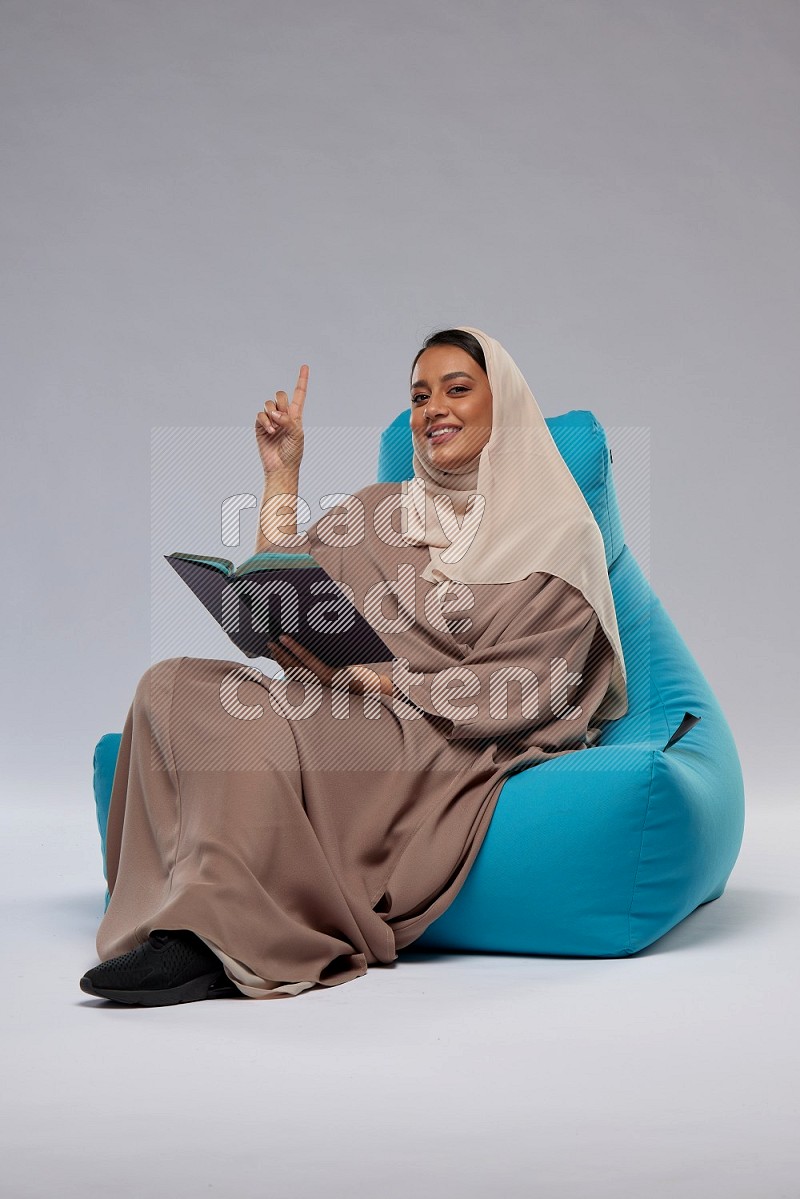 A woman sitting on a blue beanbag and reading a book